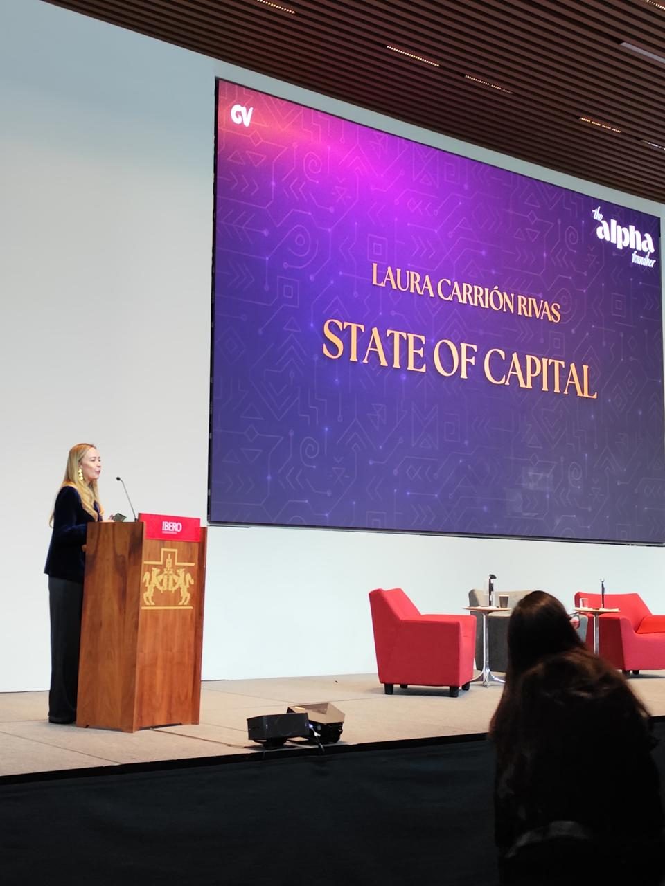 Laura Carrión Rivas en el escenario de Alpha Founder junto a la pantalla de State of Capital