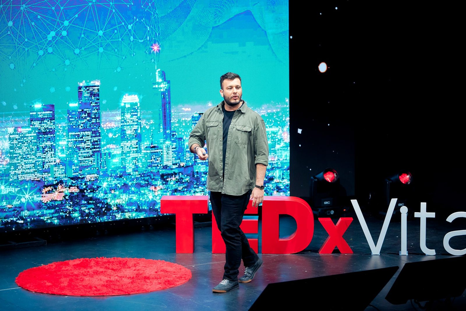 Tomás Ffrench-Davis en el escenario de TEDxVitacura, con una ciudad de noche en pantalla